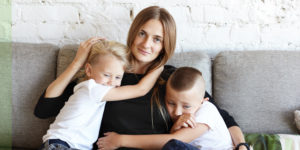caucasian woman and her two young children on a couch with a white brick wall in the background
