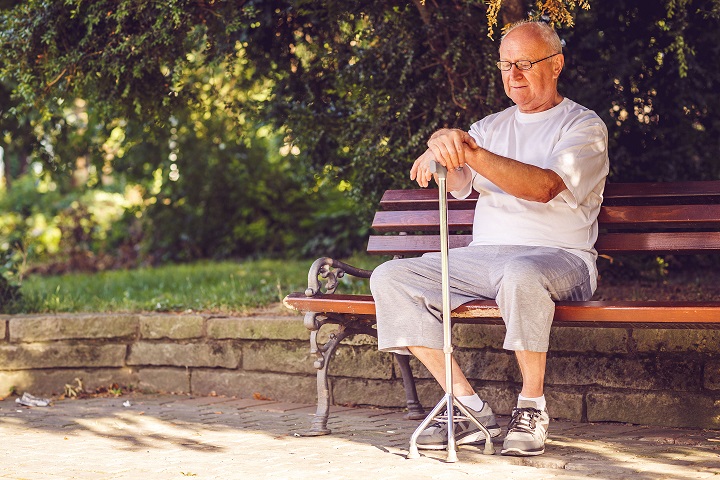 Sad elderly man with his walking stick sitting on bench in the park